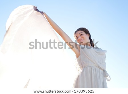 Beauty portrait view of an elegant smiling woman rising a floating silk fabric up with her arms against a bright blue sky on holiday, outdoors. Travel, beauty and lifestyle.