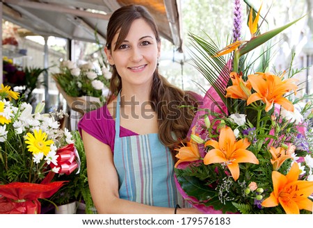 Close up portrait of a business woman florist working at her flower market shop and carrying a large bouquet of orange lilies flowers in her small business, outdoors.