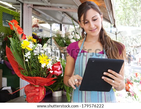 Portrait of a young business woman florist working at her flower market shop and using a digital touch screen tablet pad to work on line, outdoors. Business technology.