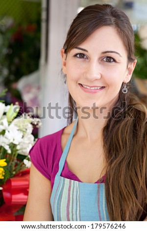 Close up portrait of a business woman florist working at her flower market stall, standing by her small business smiling at the camera, outdoors. Business lifestyle.
