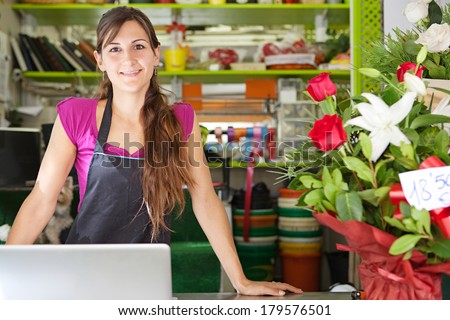 Close up portrait of a welcoming florist business woman owner proudly standing at her flower shop counter using a laptop computer and smiling. Small business technology.