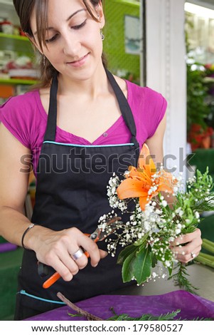 Attractive florist business owner woman working at the counter of her flower market store making a new floral arrangement during a sunny day. Small business owner.
