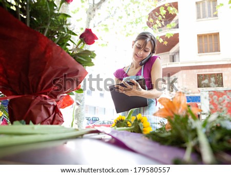 Portrait of a smiling florist business woman owner working at her flower store and ordering stock on the phone holding a clipboard, running a small business in the city.