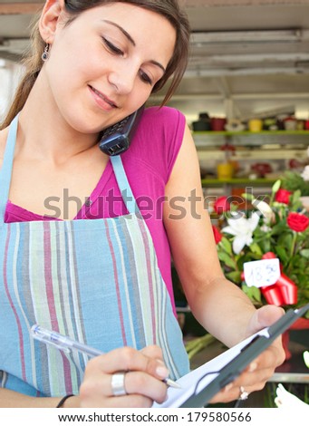 Smiling portrait of an attractive florist business woman owner at a flower shop market working and making a phone call ordering stock and running a small business, outdoors.