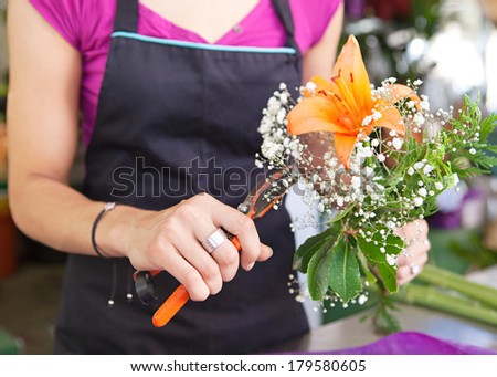 Faceless middle section hands detail view of a florist business woman owner at a flower shop market working and making a new floral arrangement. Small business owner.