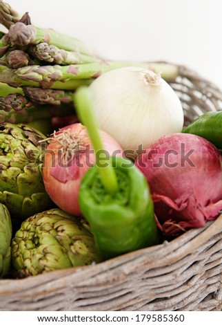 Close up view of a groceries basket full of various healthy and organic vegetables like artichockes, peppers, asparagus, onions and herbs in a home kitchen. Vegetarian food ingredients, interior.