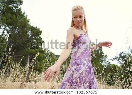 Side portrait of an attractive blond woman relaxing taking a walk in the country and being thoughtful, enjoying touching the long yellow grass in a field on holiday. Healthy and beauty lifestyle.