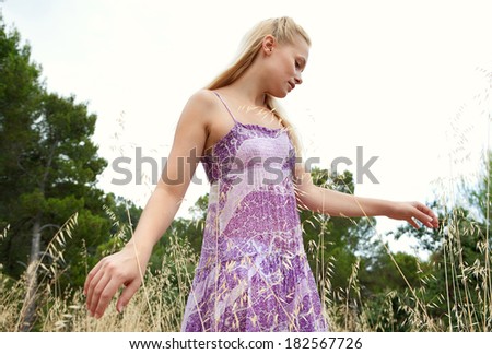 Side portrait of an attractive blond woman relaxing taking a walk in the country and being thoughtful, feeling the long yellow grass with her hands in a field on holiday. Healthy and beauty lifestyle.