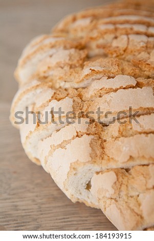 Over head close up of a home baked loaf of white bread with crunchy crust resting on a wooden kitchen table, cooling after baking, cut in slices with a golden color. Food object in home interior.