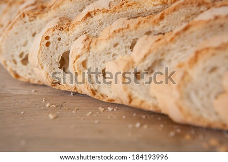 Macro close up detail of a home baked loaf of white bread with crunchy crust resting on a wooden kitchen table, cut in slices with a golden color. Food object in home interior.