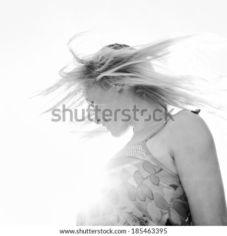 Black and white portrait of a joyful happy woman throwing her hair flying in the air against the sun shining rays filtering with flare in a spontaneous celebratory expression. Healthy lifestyle.