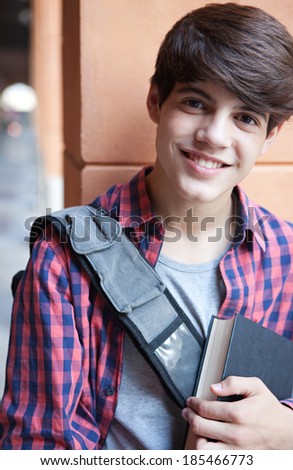 Close up portrait of an attractive teenager student boy in a college campus leaning against an old stone building wall and smiling at the camera. Student outdoors lifestyle.