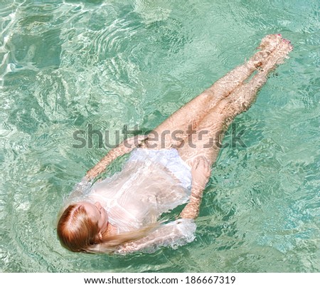 Over head view of a young woman swimming in the clear blue waters of a health spa swimming pool, relaxing on a summer holiday trip and enjoying a swim during a sunny summer day, outdoors lifestyle.