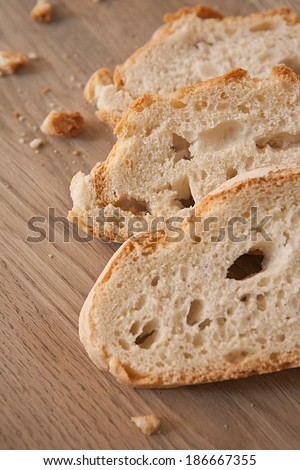 Close up detail of tempting slices of white bread with crunchy crust and bread crumbs resting on a wooden kitchen table with a golden color. Food baking in home interior, object.