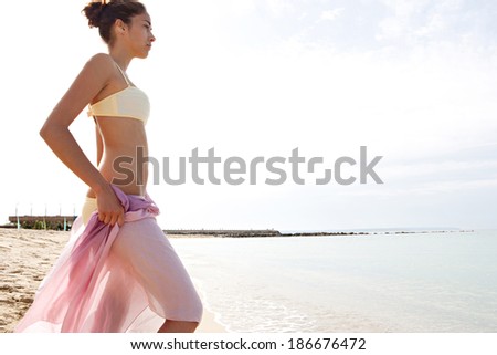 Profile view of a beautiful young woman body wrapping a silk fabric sarong around her body and contemplating the blue sea and sky during a sunny day on holiday. Travel and beauty lifestyle.