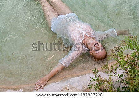 Over head beauty portrait view of a young woman relaxing in the transparent blue waters of a health spa natural swimming pool with her eyes shut, enjoying a summer holiday, outdoors healthy lifestyle.