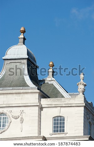 Still life detail view of a classic centenary stone building black tiles roof with decorative arches against a bright blue sky in the city of London. Architectural detail of power and status outdoors.