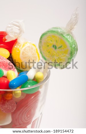 Still life of a glass container with different colorful candy sweets, fruity sticks, liquorice and jelly beans isolated on white background. Indulgence and naughty sugar and fat full food temptation.