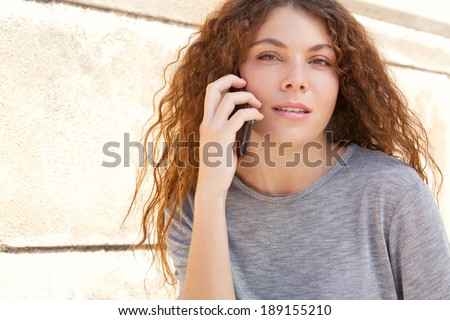 Close up portrait of an attractive professional young woman by a textured stone wall making a call on her smartphone during a sunny day outdoors. Thoughtful business woman, technology lifestyle.