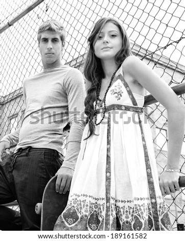 Black and white portrait of two diverse teenager friends relaxing together on a college campus sports ground looking thoughtful during a break at university. Students skateboarding outdoors lifestyle.