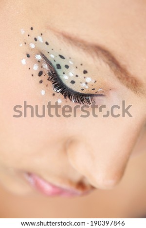 Over head close up beauty portrait of an attractive young african american black woman wearing spotted eye shadow make up cosmetics, looking down thoughtfully. Fantasy make up beauty and lifestyle.