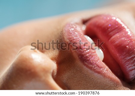 Close up lips beauty detail of an attractive african american young black woman leaning her chin on her hand while wearing glossy lipstick, smiling at the camera with healthy teeth. Beauty lifestyle.