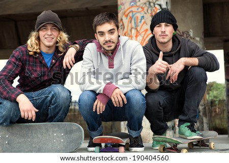 Portrait of a diverse group of teenager friends men relaxing and crouching down together with their skate boards in a skateboarding park during a fun and sporty day outdoors. Fun and sport lifestyle.