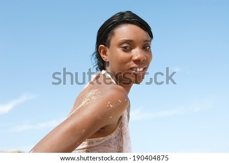 Side portrait of an attractive young african american black woman with perfect skin on beach during a summer holiday, relaxing on a sunny day against a bright blue sky, outdoors. Lifestyle and travel.