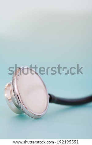 Close up detail still life view of a doctor stethoscope laying on a plain blue background in a hospital table, interior. Health and medical equipment and insurance icon with no people.