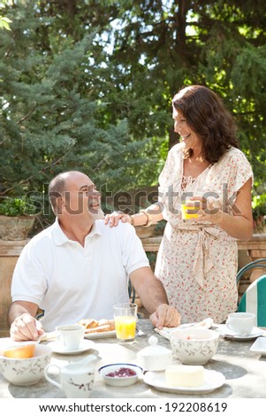 Senior couple having breakfast together at a table in a luxury hotel garden during a sunny day. Mature people eating healthy food drinking coffee and juice in each others company. Outdoors lifestyle.