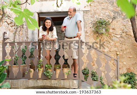 Attractive mature couple standing on a staircase in a luxury hotel holiday villa green garden on vacation, drinking a glass of wine together and smiling enjoying retirement. Outdoors senior lifestyle.