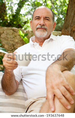 Portrait of a senior man sitting in a luxury hotel garden on holiday drinking coffee and relaxing on vacation. Mature people drinking hot beverages, outdoors. Senior people lifestyle.