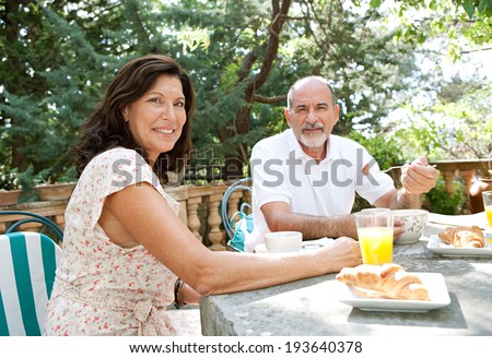 Portrait of a senior couple enjoying a healthy breakfast together in a luxury home garden on holiday. Mature people eating healthy food and enjoying each others company, outdoors. Travel lifestyle.