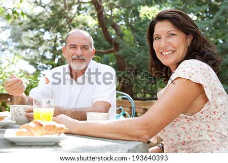 Portrait of a senior couple enjoying a healthy breakfast together in a luxury home garden on holiday. Mature people eating healthy food and enjoying each others company, smiling. Travel lifestyle.
