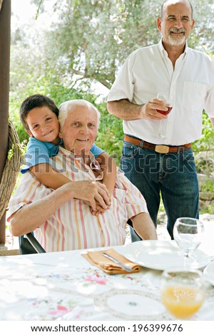 Grandfather, father and son relaxing together on vacation, sitting at a food table outdoors in a holiday villa home green garden, having fun and bonding during a sunny summer day, lifestyle.