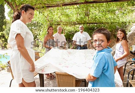 Large family group setting up a table cloth together in teamwork, getting ready for eating lunch outdoors during a sunny day on holiday in a summer villa vacation home garden, relaxing lifestyle.