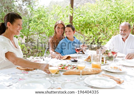 Attractive joyful family members sitting at a lunch table in a holiday villa green garden relaxing on a summer vacation during a sunny day. Family outdoors living and healthy eating lifestyle.