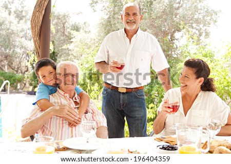 Portrait of a joyful family gathering around a healthy lunch food eating table outdoors during a summer holiday in a vacation garden home. Fun, love and affection family enjoying the sun, lifestyle.