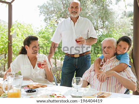 Group of joyful family members enjoying a Spanish tapas meal in a villa green garden while on a holiday in a summer home, eating and drinking together during a summer day, portrait outdoors.