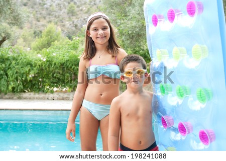 Colorful portrait of a brother and sister standing together at the edge of a swimming pool, smiling and holding a blue inflatable bed during a summer holiday in a hotel. Active vacation lifestyle.