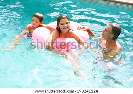 Father and children playing games and having fun in a holiday swimming pool, swimming and sharing an inflatable pink ring during a sunny summer day. Family activities and fun outdoors, lifestyle.