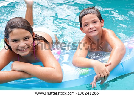 Portrait of two brother and sister children swimming together in a blue pool and sharing an inflatable lilo while enjoying a summer holiday in the sun. Active children and family vacation lifestyle.