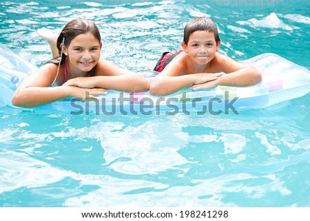Portrait of two brother and sister children swimming together in a blue pool and sharing an inflatable lilo while enjoying a summer holiday in the sun. Active children and family vacation lifestyle.