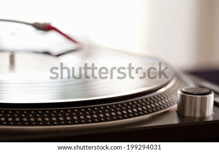Close up still life detail view of a DJ record player needle touching the groove of the album, playing against a bright light in a music club, interior. Musical hobbies. Equipment at work.