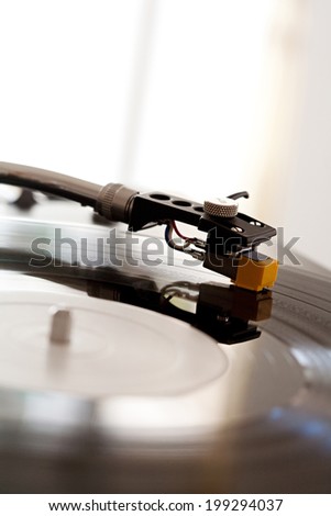 Close up still life detail view of a DJ record player needle touching the groove of the album, playing music against a bright window in a music club, interior. Musical hobbies and interests.