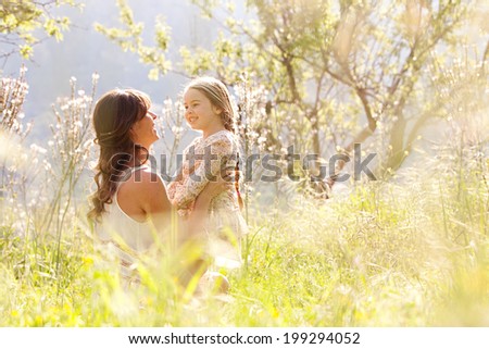 Young mother and child daughter together hugging and smiling sitting and relaxing in a golden field of sunshine and spring flowers while on a summer holiday Family activities and outdoors lifestyle Young mother and child daughter together hugging and smiling sitting and relaxing in a golden field of sunshine and spring flowers while on a summer holiday Family activities and outdoors lifestyle