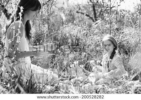 Black and white portrait of a mother and daughter sitting together in a sunny field of flowers having a picnic and enjoying a summer holiday in nature. Eating and relaxing family activities lifestyle.