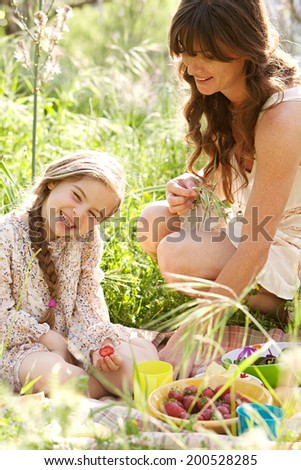 Close up portrait of a young mother and daughter relaxing together having a picnic in a green garden eating healthy food, laughing having fun. Family activities and healthy eating lifestyle, outdoors.