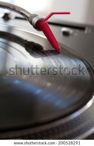 Close up detail view of a record player with a red needle touching the groove of a vinyl album playing music, interior. Still life professional musical equipment objects.