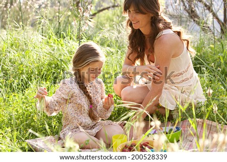 Close up portrait of a mother and daughter relaxing together having a picnic in a lush green garden eating healthy food, smiling having fun. Family activities and healthy eating lifestyle, outdoors.